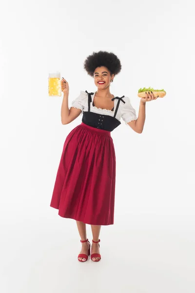 Щаслива афроамериканська офіціантка в традиційному костюмі з пивом і хот-догом на білому — стокове фото
