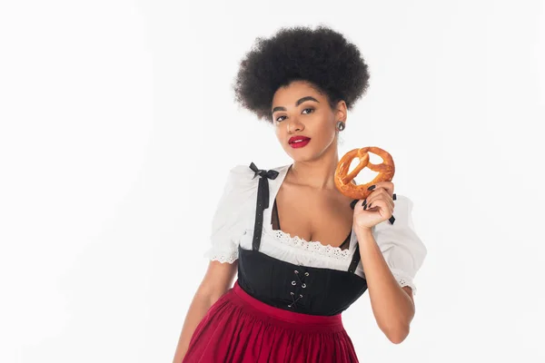 Pretty african american bavarian waitress in oktoberfest outfit holding delicious pretzel on white — Stock Photo