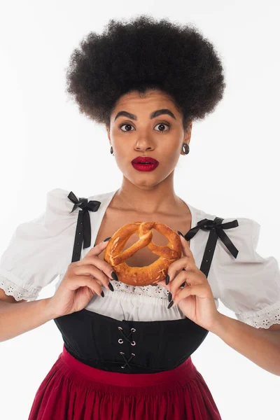 Вражена афроамериканська офіціантка в автентичному баварському костюмі зі смачним кренделем на білому — стокове фото