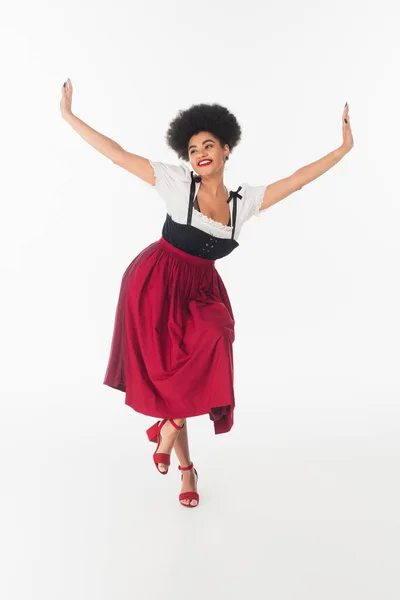 Alegre africano americano bavarian camarera en elegante dirndl realización oktoberfest danza en blanco - foto de stock