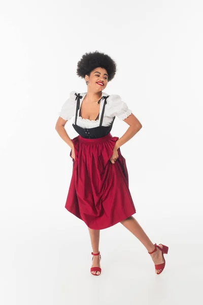 Overjoyed african american oktoberfest waitress in traditional bavarian costume dancing on white — Stock Photo