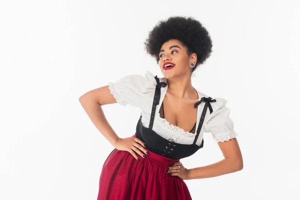 Alluring african american oktoberfest waitress in dirndl looking away with hands on hips on white — Stock Photo