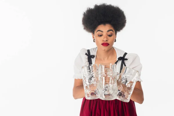 Discouraged african american bavarian waitress in oktoberfest outfit with empty beer mugs on white — Stock Photo