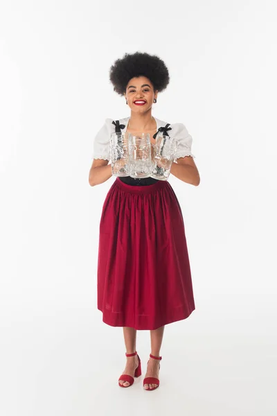 Happy african american waitress in bavarian costume with empty beer mugs on white, oktoberfest — Stock Photo