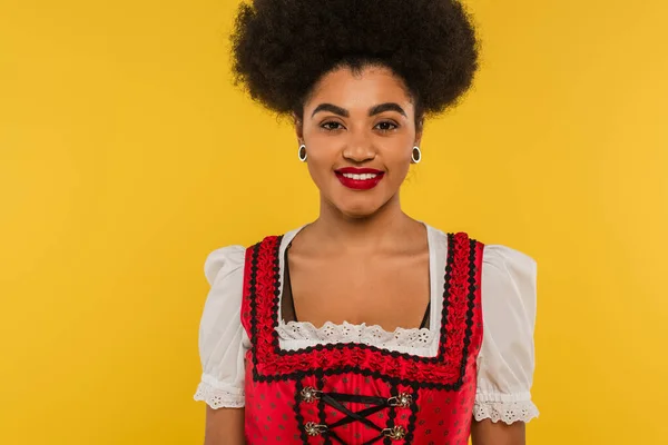 Attractive african american bavarian waitress in traditional costume looking at camera on yellow — Stock Photo