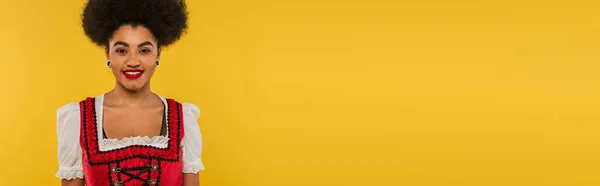 Junge afrikanisch-amerikanische Oktoberfestkellnerin im Dirndl lächelt auf gelbem Transparent in die Kamera — Stockfoto