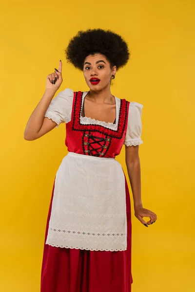 Excitée serveuse afro-américaine en costume bavarois traditionnel montrant signe d'idée sur jaune — Photo de stock