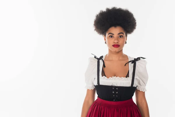 Young african american bavarian waitress in traditional dirndl costume looking at camera on white — Stock Photo