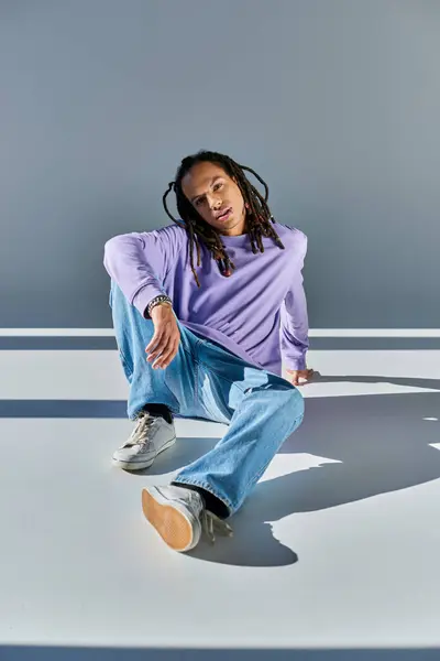Handsome african american man in sweatshirt with dreadlocks sitting on floor and looking at camera — Stock Photo