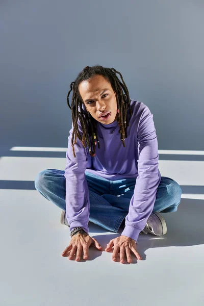 Joven afroamericano hombre en sudadera púrpura con rastas y labio perforado mirando a la cámara - foto de stock