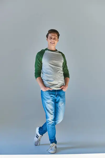 Jeune homme souriant en casual manches longues et jeans souriant à la caméra posant avec les mains dans les poches — Photo de stock