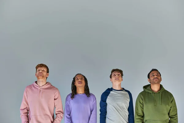 Four smiling young men in casual bright attire looking up on grey backdrop, cultural diversity — Stock Photo