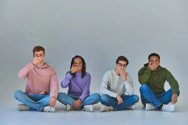 Cuatro amigos multiculturales sentados con las piernas cruzadas y cubriendo bocas, diversidad cultural - foto de stock