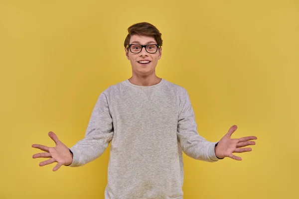 Cheerful surprised man in casual attire and glasses raising hands with open palms on yellow backdrop — Stock Photo