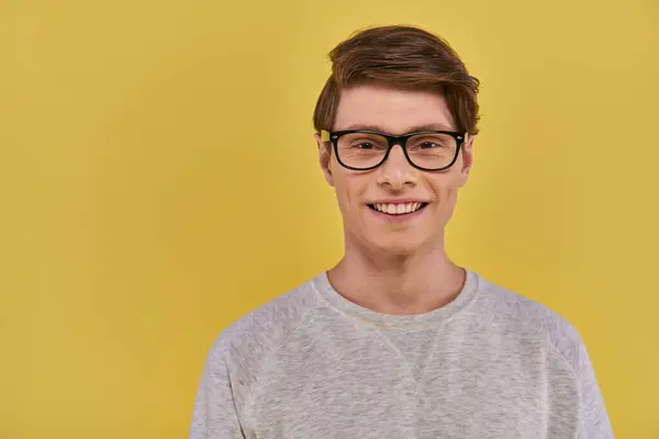 Fröhlicher junger Mann in weißer Kleidung mit Brille, der vor gelbem Hintergrund aufrichtig in die Kamera lächelt — Stockfoto