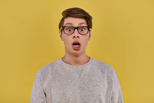 Surprised young man in casual comfortable attire and glasses looking at camera with open mouth — Stock Photo