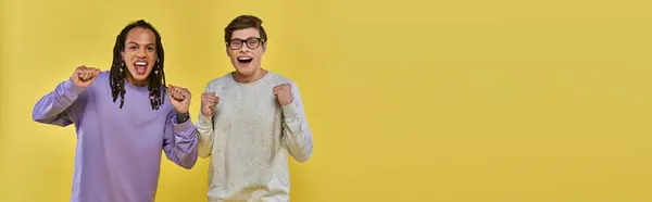 Amigos multiculturales alegres en atuendo casual sonriendo con los puños en alto, cultural diversa, bandera - foto de stock