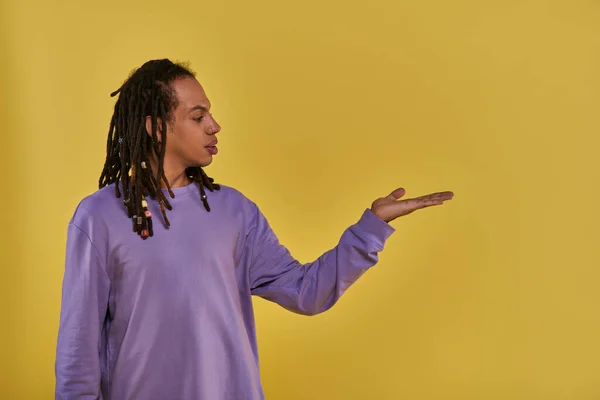 Confused african american man in purple sweatshirt with dreadlocks holding hand empty palm up — Stock Photo