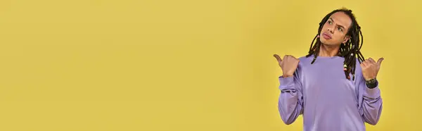 Perplesso giovane uomo con i pollici dreadlocks indicando modi diversi su sfondo giallo, banner — Foto stock
