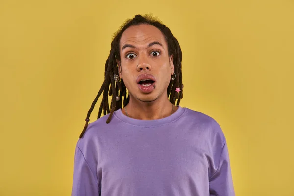 Close up surprised man in purple sweatshirt with pierced lip and dreadlocks on yellow background — Stock Photo