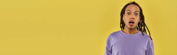 Surprised african american man in purple sweatshirt with pierced lip on yellow background, banner — Stock Photo