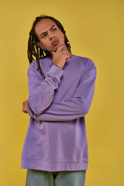 Nachdenklicher junger Mann in lila Sweatshirt denkt nach oben und schaut auf gelbem Hintergrund weg — Stockfoto