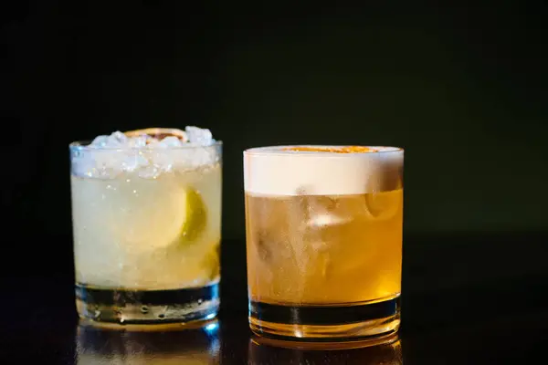 Sophisticated whiskey sour and exotic caipirinha on black background, object photo, concept — Stock Photo