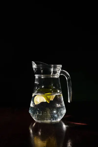 Enorme sete dissetante e brocca fresca di acqua limpida con piccole fette di limone su sfondo nero — Foto stock