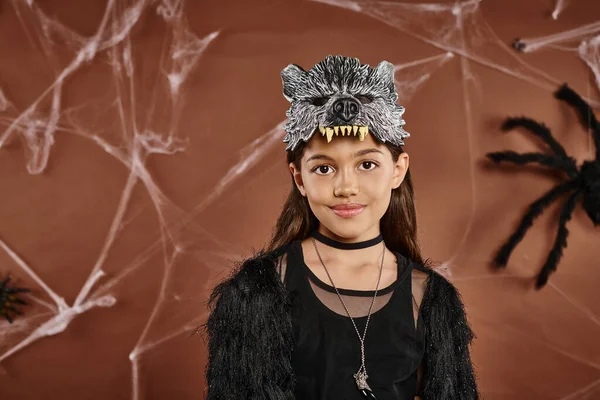 Carino ragazza in abito nero con maschera di lupo su sfondo marrone, primo piano, concetto di Halloween — Foto stock