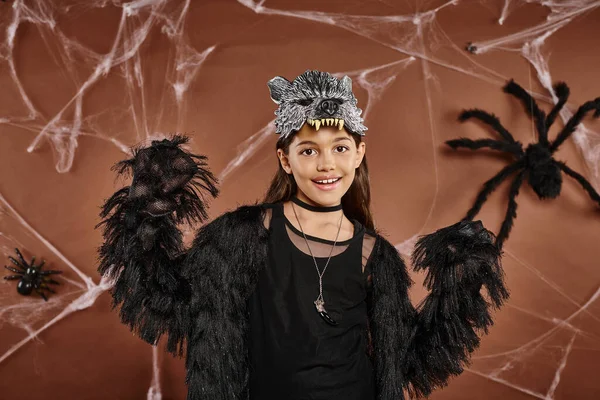 Menina pré-adolescente alegre posando em roupa de Halloween preto e máscara de lobo no fundo marrom — Fotografia de Stock