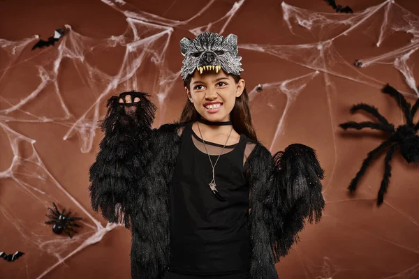 Close up of preteen girl in black attire and wolf mask scaring with raised hands, Halloween concept — Stock Photo