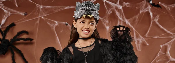 Primer plano de niña preadolescente en traje negro y máscara de lobo asustando con las manos levantadas, concepto de Halloween - foto de stock