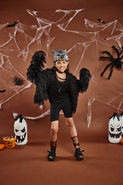 Niña preadolescente en traje negro con cubo de dulces y linternas sobre fondo marrón, Halloween - foto de stock