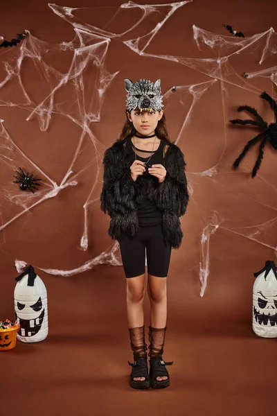 Ragazza carina in abbigliamento eco-pelliccia con maschera di lupo in piedi ancora su sfondo marrone, concetto di Halloween — Stock Photo