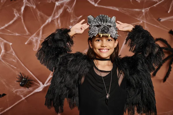 Cerrar sonriente niña preadolescente con las manos levantadas en traje de piel sintética negro, concepto de Halloween - foto de stock