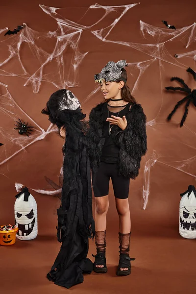 Preteen girl holding Halloween toy on brown backdrop with spiders, web and lanterns, Halloween — Stock Photo