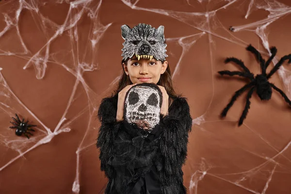Smiling girl in wolf mask and black attire hugging Halloween toy skeleton, Halloween concept — Stock Photo