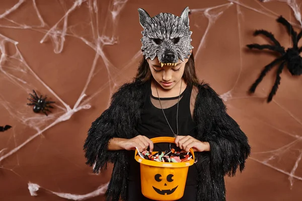 Primer plano preadolescente chica mirando su cubo de dulces en marrón telón de fondo con tela de araña, Halloween - foto de stock
