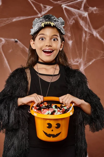 Portrait of happy girl in wolf mask showing her bucket of sweets, Halloween concept — Stock Photo