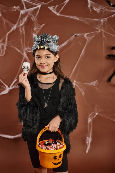 Close up smiley preteen menina com balde de doces segurando um crânio de Halloween, conceito de Halloween — Fotografia de Stock