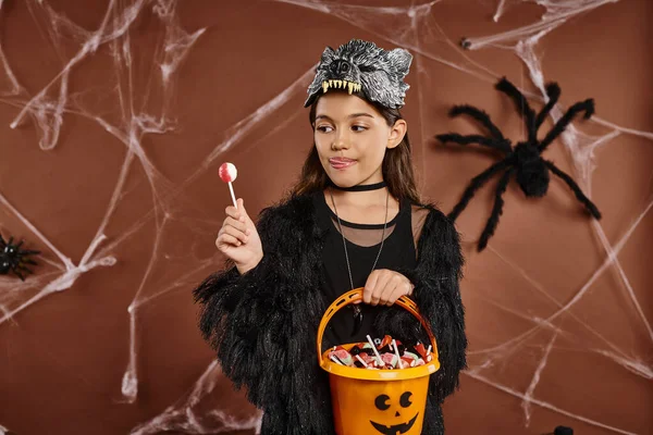 Cerca de niña preadolescente con balde de caramelo y piruleta en la mano, concepto de Halloween - foto de stock