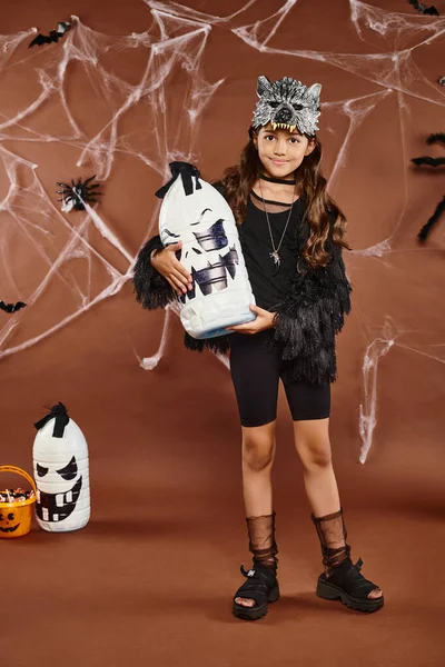 Sorridente preteen menina detém lanterna Halloween no fundo marrom com web, aranhas e morcegos, Halloween — Fotografia de Stock
