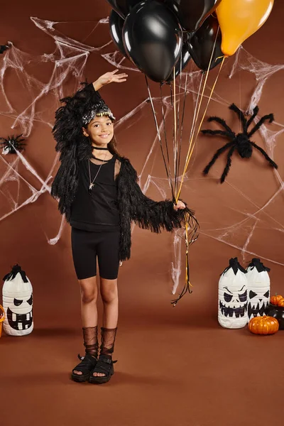 Fröhliches Mädchen hält schwarze und orangefarbene Luftballons und berührt sie mit der Hand, Halloween-Konzept — Stockfoto