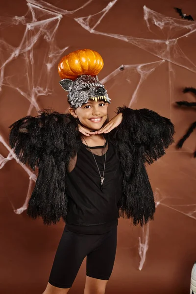Cerca de niña preadolescente sonriente con calabaza en la cabeza y las manos bajo la barbilla, Halloween - foto de stock