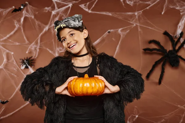 Smiley preteen girl holding pumpkin in her hands on brown backdrop, Halloween concept — Stock Photo