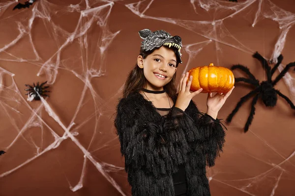 Preteen girl holding pumpkin in her hands aside on spiderweb brown backdrop, Halloween concept — Stock Photo