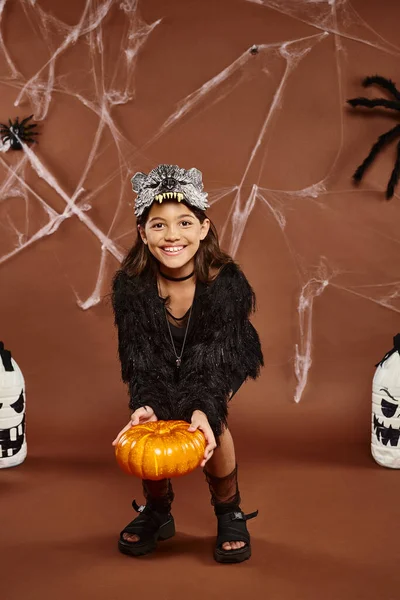 Preteen girl bends over with pumpkin in hands with lanterns and spiders on backdrop, Halloween — Stock Photo
