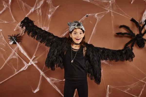 Chica feliz con los brazos abiertos en traje de piel sintética negro con tela de araña sobre fondo marrón, Halloween - foto de stock
