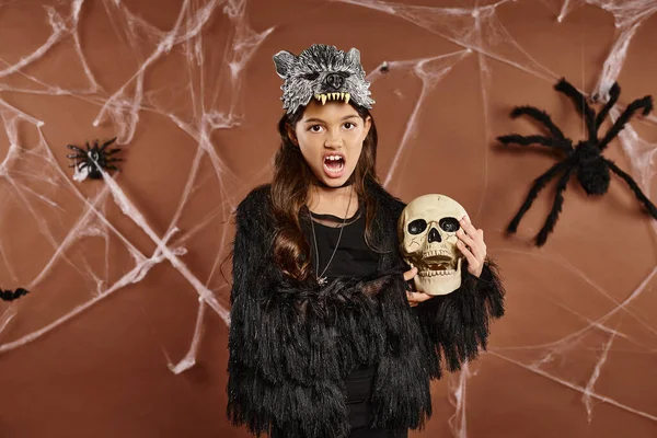 Close up surprised girl with open mouth holds skull with brown backdrop, Halloween concept — Stock Photo