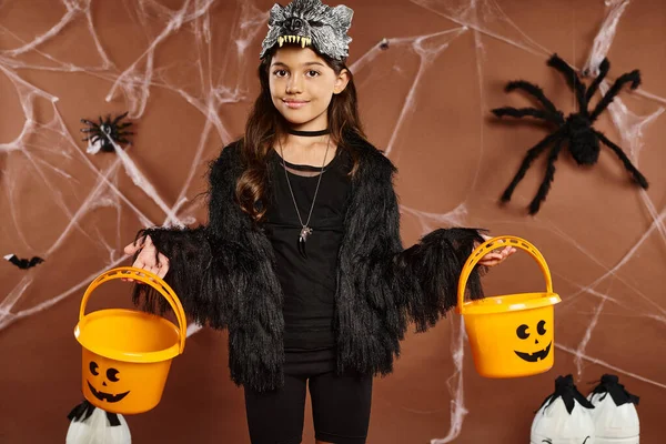 Smiley kid in wolf mask with two pumpkin buckets on brown background with webs, Halloween, close up — Stock Photo
